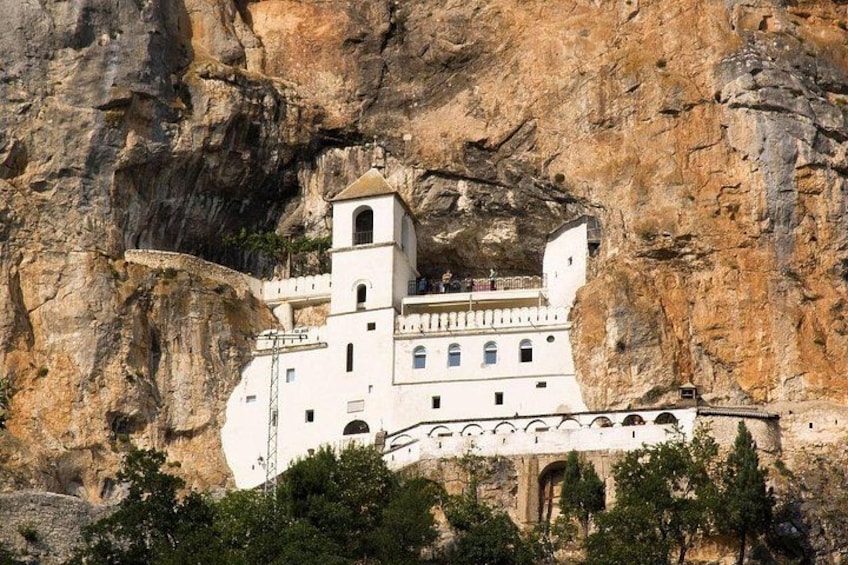 A white building with a bell tower, perched on a cliff. 1
