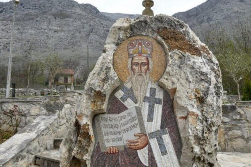 A mosaic of a religious figure on a stone structure with a mountainous background. 4