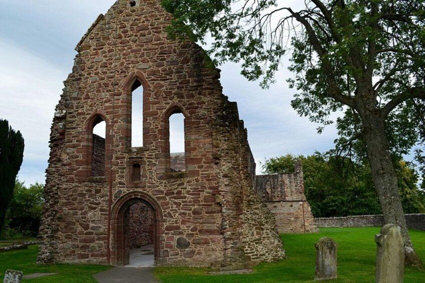 An ancient stone structure with arched windows and a central doorway, surrounded by grass and trees. 2