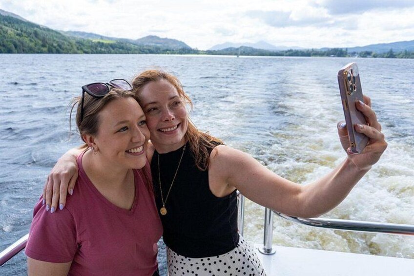 Two people on a boat taking a selfie with a lake and mountains in the background. 3