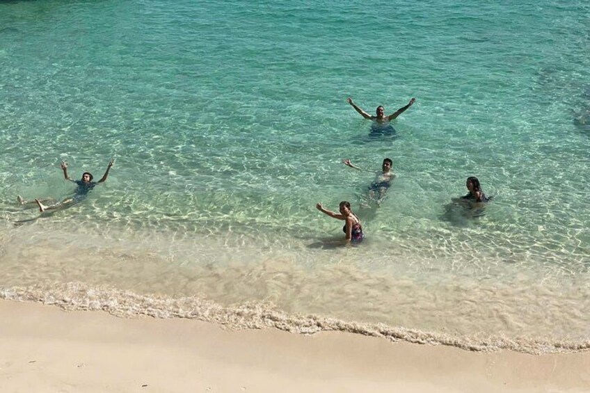 Una spiaggia con acque cristalline turchesi e persone che nuotano e giocano in un tratto poco profondo. 4