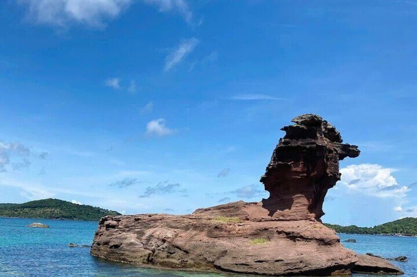 A rock formation with a unique shape, surrounded by clear blue water and distant hills. 4