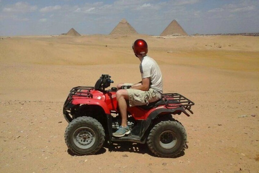 Una persona conduciendo un vehículo todo terreno en un desierto con pirámides al fondo. 2