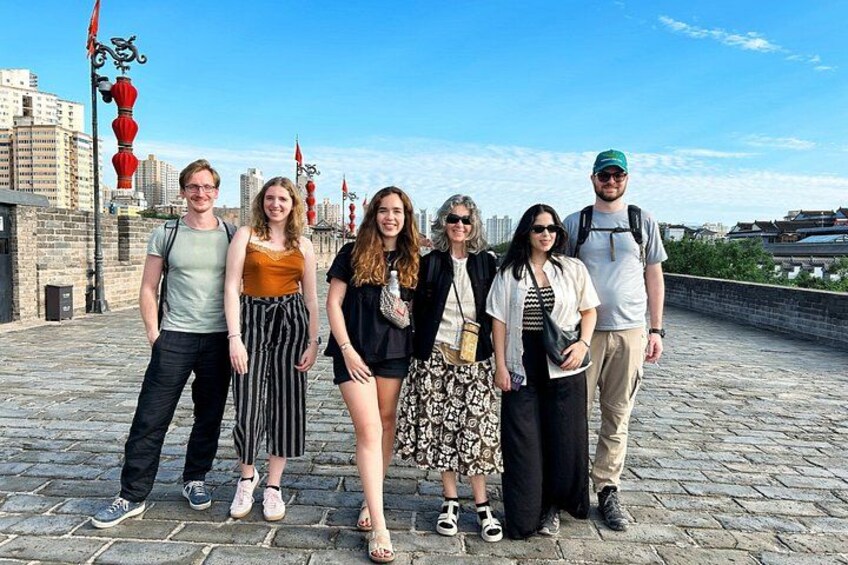 Un groupe de personnes se tient sur un pont de pierre, avec des bâtiments en arrière-plan. 3
