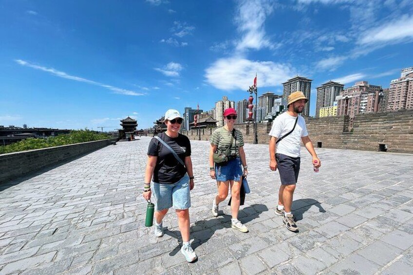 Three people walking on a paved pathway with a cityscape in the background. 5