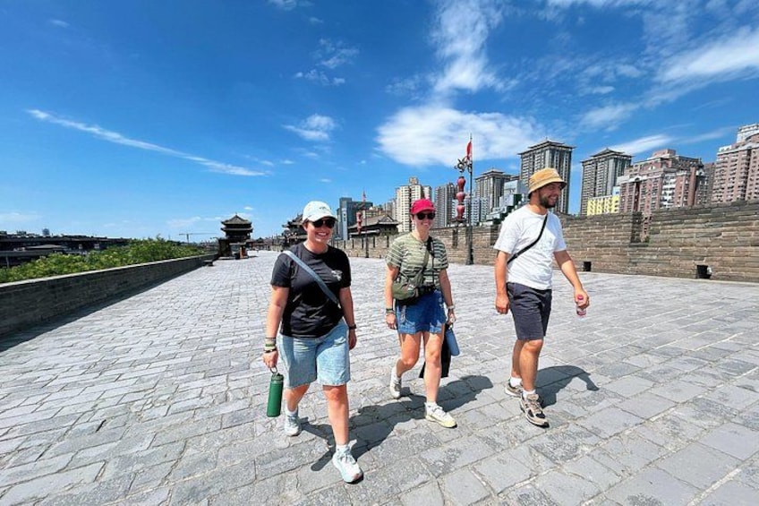 Three people walking on a paved pathway with a cityscape in the background. 5