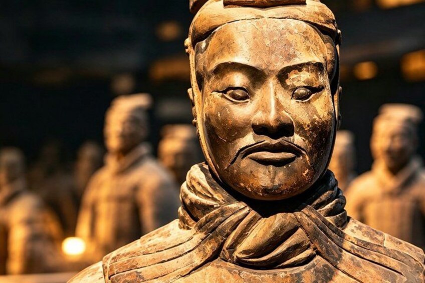Une statue en terre cuite ornée de motifs complexes, placée sur un fond composé d’autres statues similaires. 1
