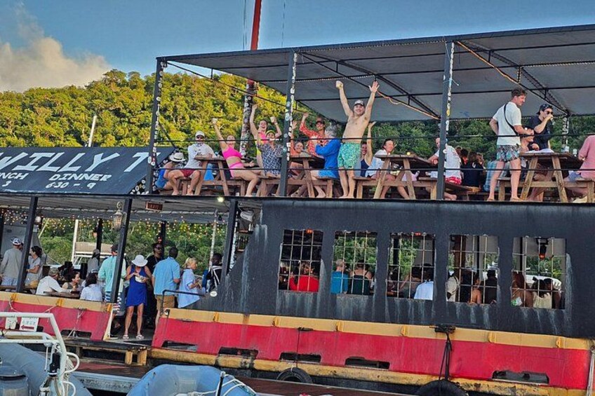 A boat with people on the deck, a sign that reads 'WILLY TINCH DINNER,' and a forested hillside in the background. 2