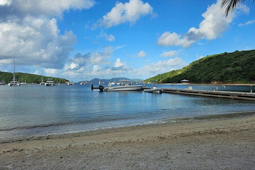 A calm waterfront with boats docked, a sandy beach, and lush green hills in the background. 5