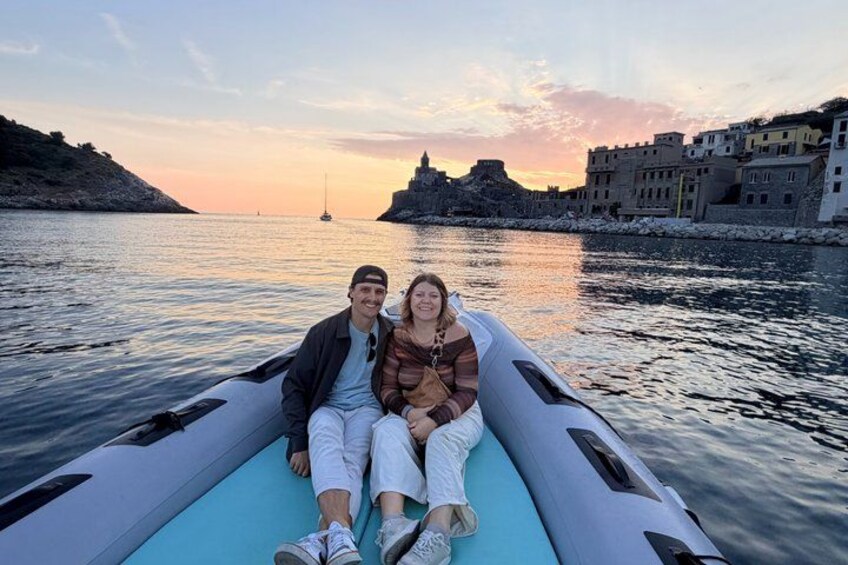 Dos personas en un bote en un cuerpo de agua con un atardecer y edificios al fondo. 2