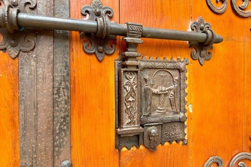A wooden door with an ornate metal latch and a decorative plaque. 4
