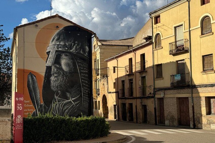 A mural of a historical figure on a building, a street, and traditional architecture. 1