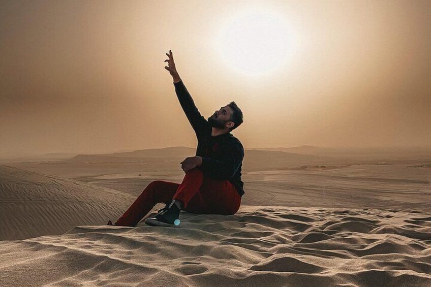 A person sitting on sand dunes with a desert landscape in the background. 4