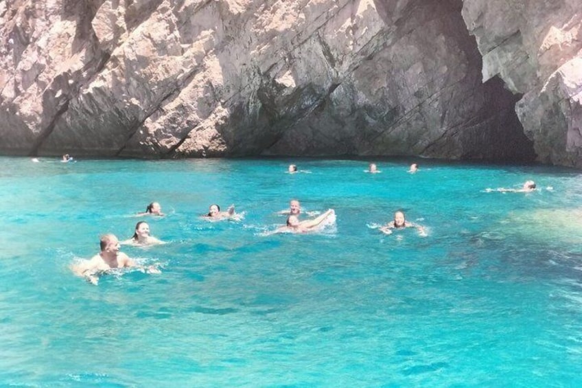 People swimming in clear blue water with rocky cliffs in the background. 4