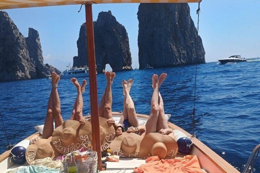 A boat with people sunbathing, a rocky coastline, and a clear blue sea. 1