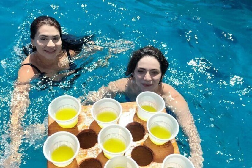 Two people in a pool with a tray of yellow drinks. 3