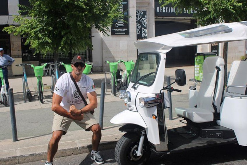 A man standing next to a white golf cart on a street with green trash bins and a building in the background. 3
