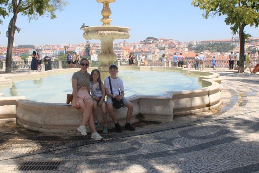 A fountain with a circular basin, surrounded by a paved area with trees. 3