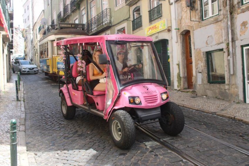 A pink trolley on a cobblestone street with buildings in the background. 2