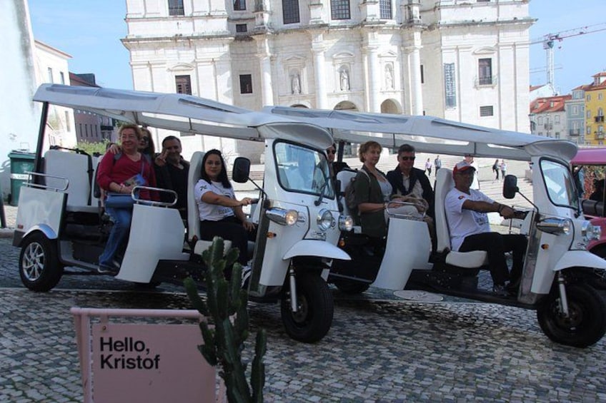 A group of people on a white three-wheeled vehicle, parked on cobblestone street. 5