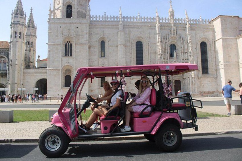 A pink golf cart with passengers, parked in front of a large historic cathedral. 4