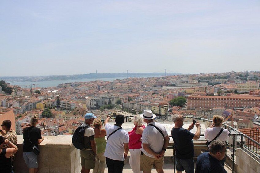 A group of people standing on a viewing platform overlooking a cityscape with buildings and a bridge in the distance. 4
