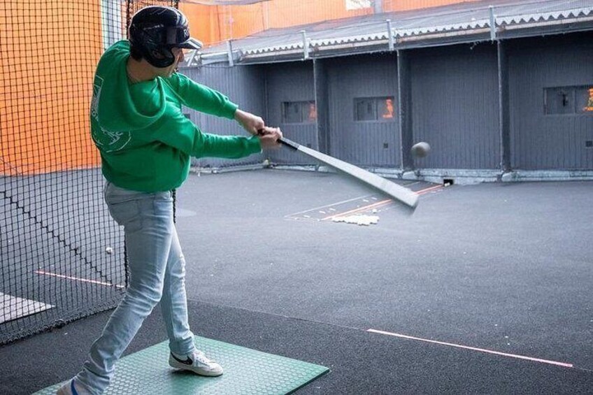 A person practicing baseball swings in an indoor batting cage. 3