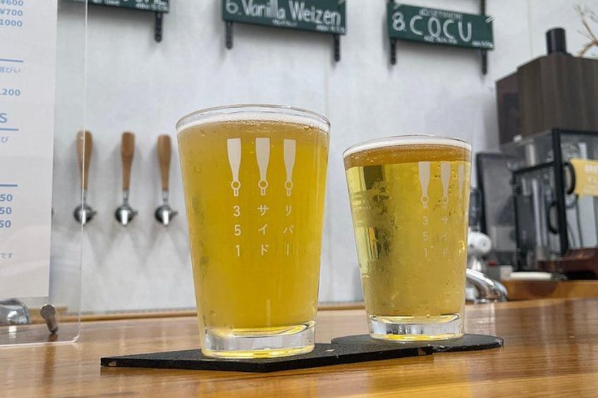 Two glasses of beer on a coaster, a beer tap, and a coffee machine in the background. 1