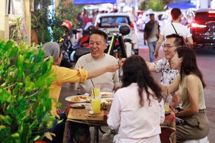 Un groupe de personnes est réuni autour d’une table en plein air, le soir, avec des chaises et des boissons. 4