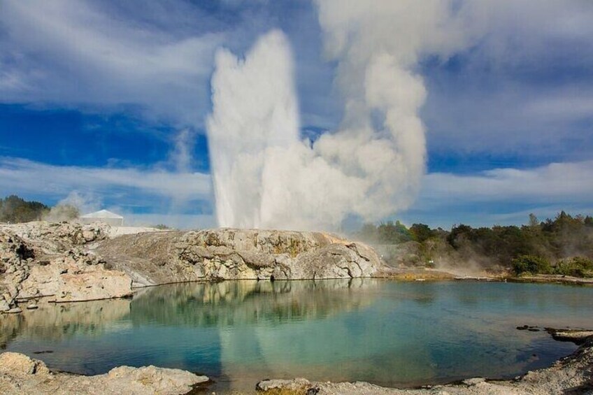 A geyser with a pool of water in the foreground, steam rising from the geyser, and a rocky landscape in the background. 2