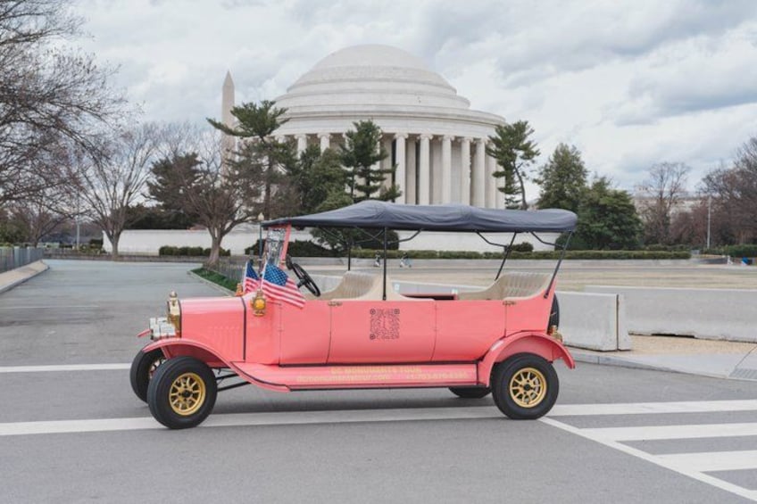 A vintage red car parked in front of a large white building with columns. 5