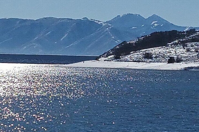 A body of water reflecting sunlight, a snow-covered shoreline, and distant mountains. 2