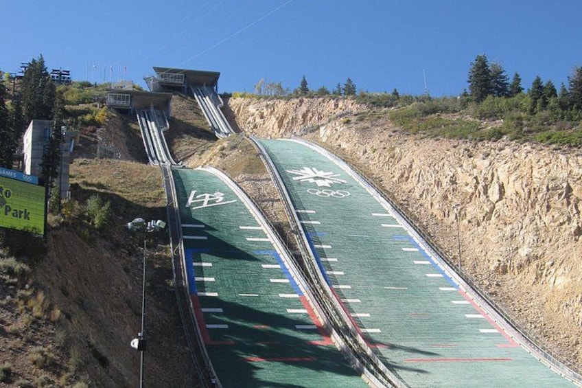 A steep, winding road with a green surface and white markings, surrounded by a rocky hillside and sparse vegetation. 4