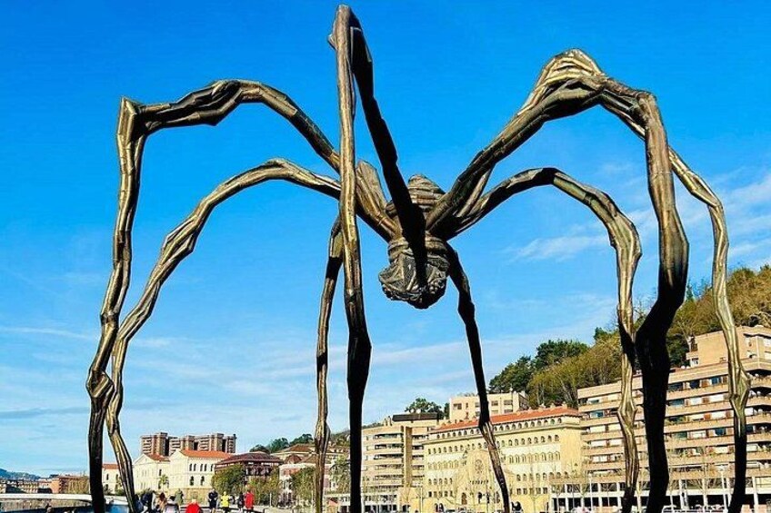 A sculpture of a spider in an outdoor setting with buildings in the background. 4