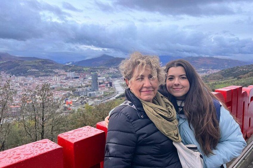 Two people standing on a red structure with a cityscape in the background. 3