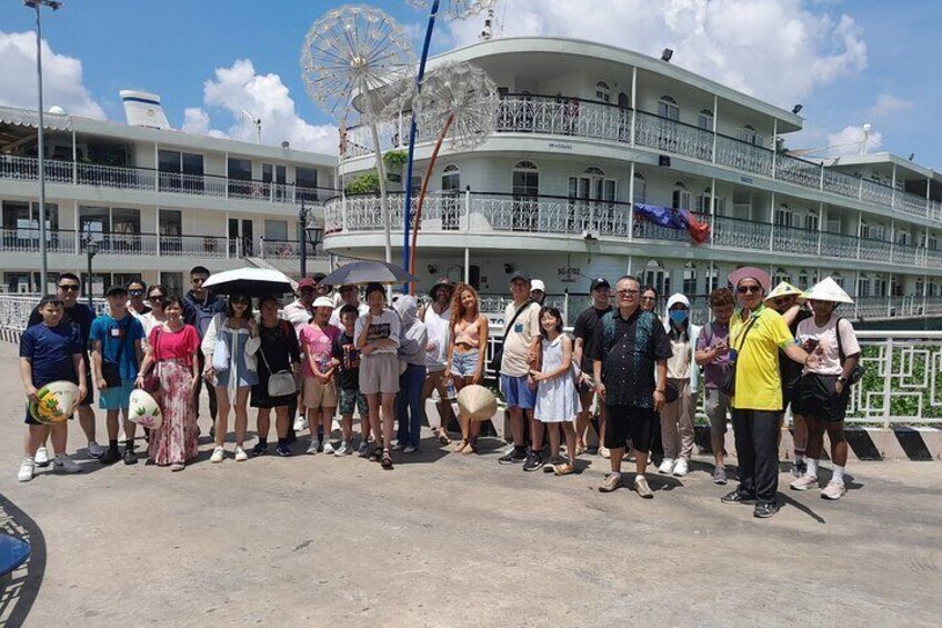 A group of people standing in front of a large white building with balconies and a Ferris wheel in the background. 3