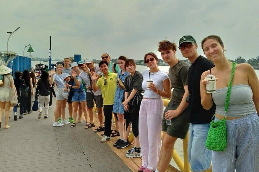 A group of people standing on a wooden boardwalk by a body of water. 5