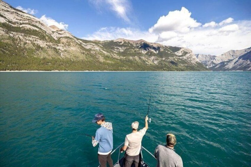Trois personnes sont en train de pêcher sur un lac paisible, avec des montagnes en arrière-plan. 4