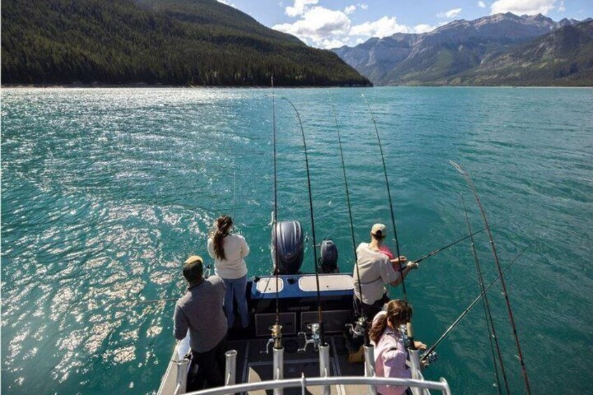 Un groupe de personnes pêchant à bord d’un bateau sur un lac turquoise, entouré de montagnes. 5