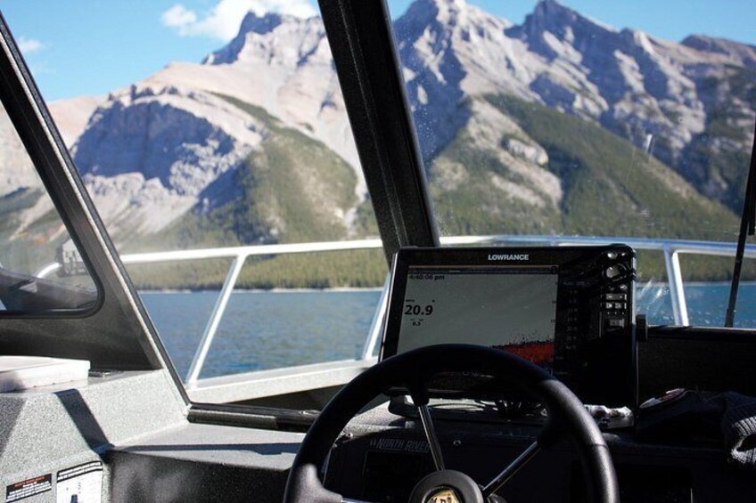 Interior de un barco con timón, pantalla de navegación y vistas a montañas y agua. 3
