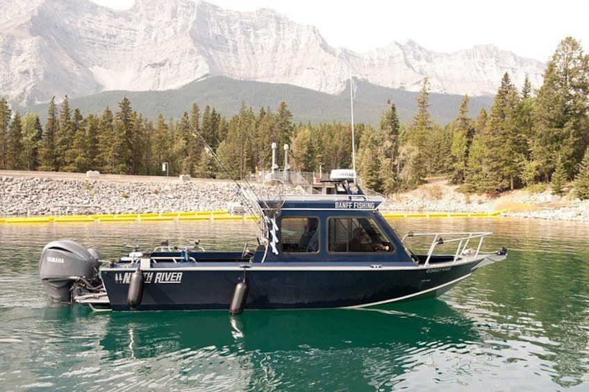 A boat named 'MAMMOTH RIVER' with 'BANK FISHING' written on it, docked near a rocky shore with mountains in the background. 5