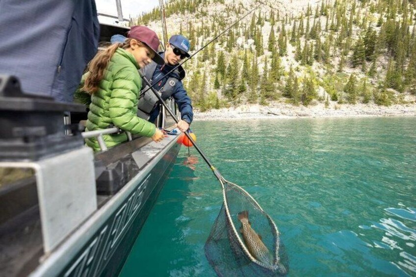 Deux personnes pêchent depuis un bateau sur un lac aux eaux claires, dont les rives sont bordées d’une forêt. 3