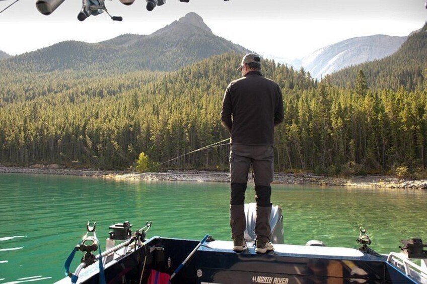 Un hombre pesca desde un bote con una cadena montañosa boscosa al fondo. 5