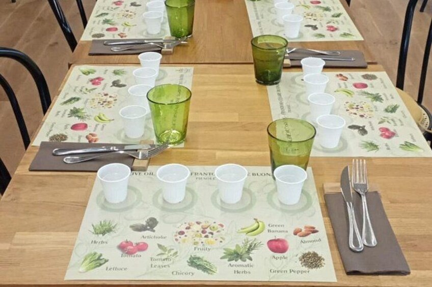Een gedekte tafel met witte bekers, groene glaasjes en een placemat met plantenafbeeldingen. 4