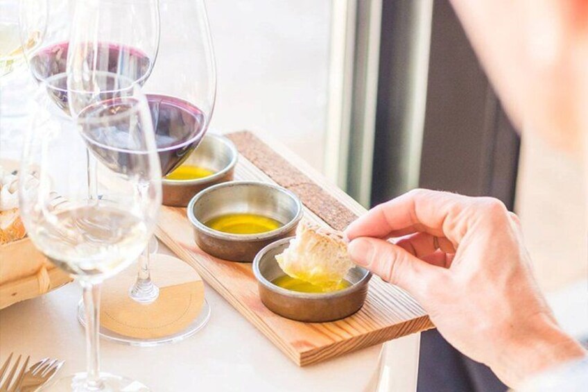 A person holding a piece of bread with a dipping sauce, with wine glasses and bowls of sauce on a table. 3