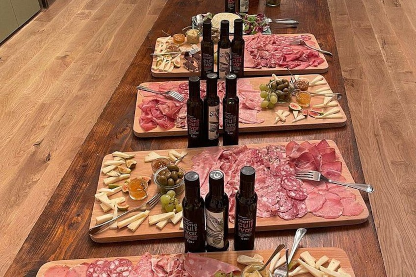 A wooden table with multiple charcuterie boards, each with various meats, cheeses, and olives, accompanied by bottles of wine. 2