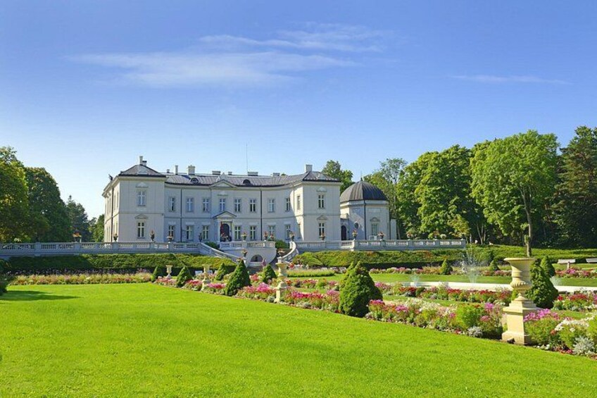 A large, classical building with a symmetrical facade, surrounded by manicured gardens and a clear blue sky. 1