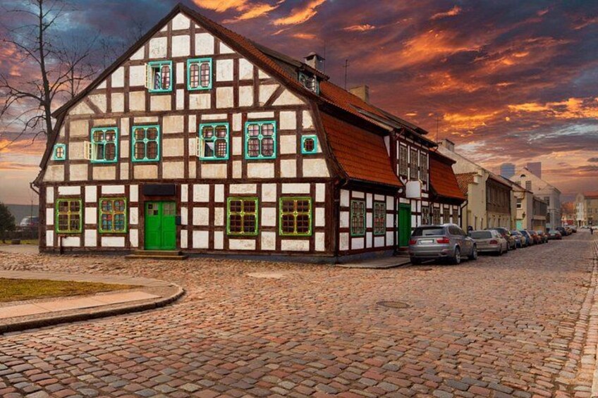 A traditional half-timbered building with a green door, parked cars along a cobblestone street, and a sunset sky. 5