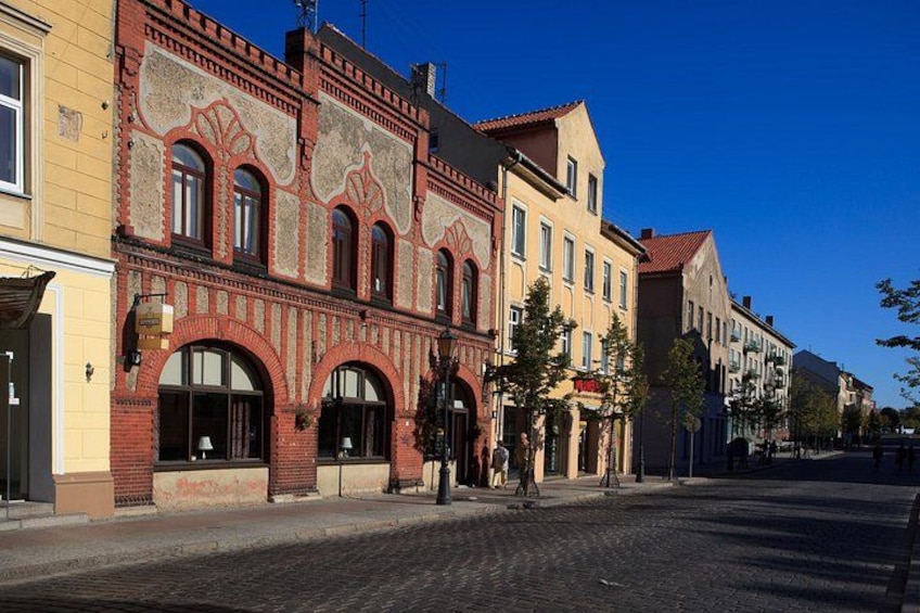 A cobblestone street lined with historic buildings, a clear blue sky, and a few trees. 3