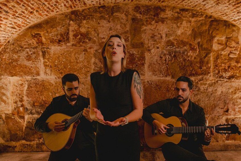 Three people playing guitars in front of a stone wall. 1